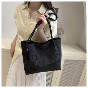 Close-up of black lace tote bag with floral patterns, tassels, and woven handle details