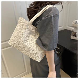 Close-up of white hollow-out woven straw tote bag with lace-like texture and gold hardware