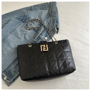 Detail of black quilted tote bag with triangle stitching and gold geometric lock