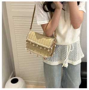 Close-up of beige woven straw bag featuring decorative seashell charms and tassels