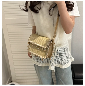 Detail of hand-woven straw crossbody bag featuring delicate lace edges and shell pendants