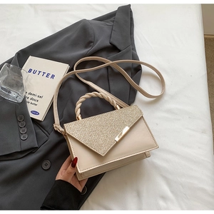 Detail of a beige handbag with golden sequin flap and twisted handle on a grey blazer