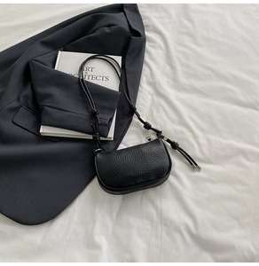 Dettaglio della pelle martellata nera su una borsa a tracolla semicircolare con nodo