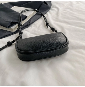 Gros plan sur le cuir grainé noir et le détail du nœud sur la bandoulière du sac