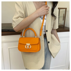 Détail d'un sac bandoulière orange vif avec fermoir doré porté par un mannequin chic