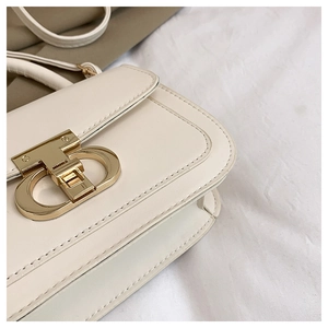 Détail rapproché du sac en cuir crème avec fermoir en métal doré en forme de T chic