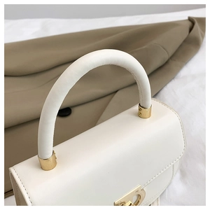 Détail d'un sac à main blanc en cuir avec un fermoir doré en forme de fer à cheval