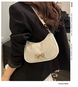 Detail of white woven hobo bag with a gold bow buckle on a model in a black blazer