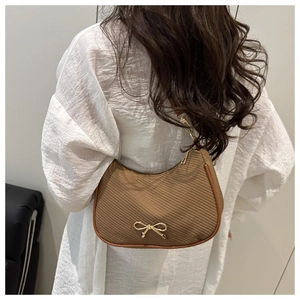 Close-up of brown woven underarm bag with gold bow hardware shown on model shoulder