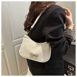 Side view of beige woven underarm bag with gold bow clasp on a female model