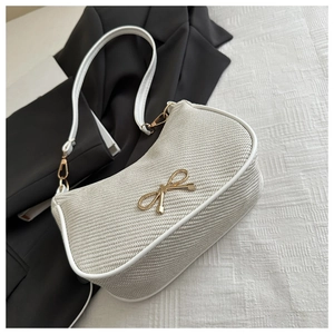Close-up of cream shoulder bag featuring woven texture and golden bow buckle