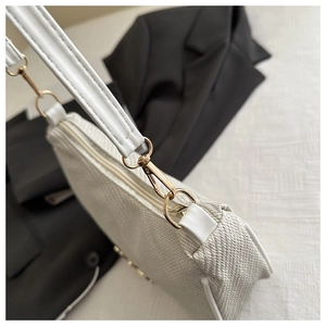 Close-up of white woven texture shoulder bag featuring gold hardware and leather strap