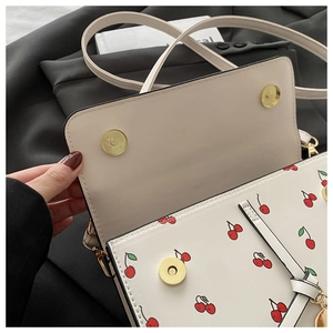 Détail du sac en cuir blanc avec imprimé cerises et fermoirs aimantés dorés