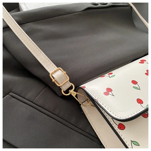 Détail du motif cerise sur le sac en cuir blanc avec finitions dorées brillantes