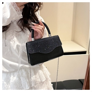 Close-up of black glitter evening bag with silver chain strap held by a model