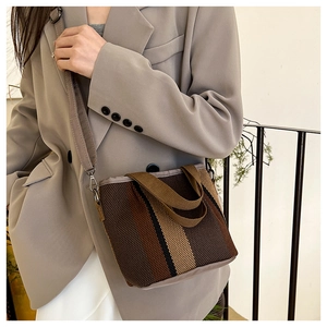 Detailed close-up of a striped canvas bucket bag worn by a model in a minimalist setting