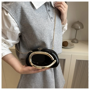 Detail of black acrylic shell clutch bag featuring a gold metal ring and chain strap