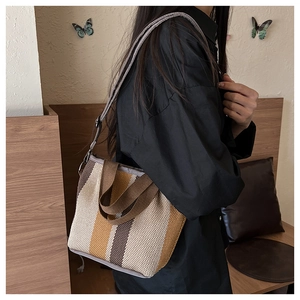 Detailed side view of a striped canvas crossbody bag with adjustable nylon shoulder strap