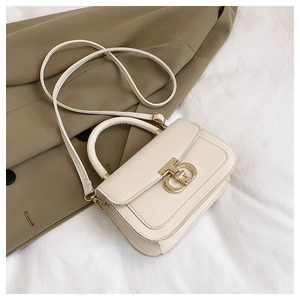 Détail d'un sac bandoulière crème avec fermoir doré, texture lisse et poignée en arc
