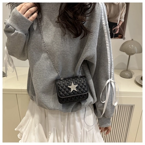 Détail du sac matelassé noir à chaîne avec étoile argentée sur une tenue grise
