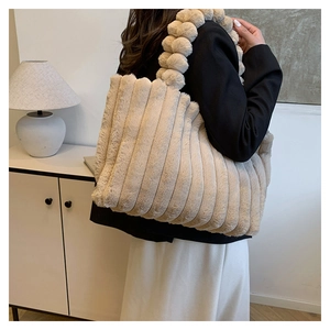 Detail of plush tote bag showing vertical stripe texture and fluffy pom-pom shoulder strap