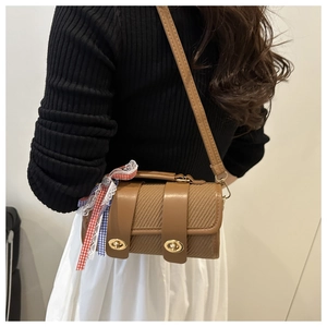 Detail of a brown woven cylindrical shoulder bag with gold turn-lock and ribbon charm