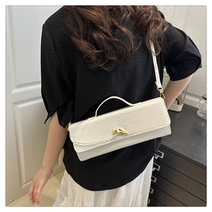 Detailed view of white crocodile pattern baguette bag with gold twist lock on model