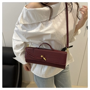 Detail of wine red crocodile embossed leather handbag with gold knot hardware and strap