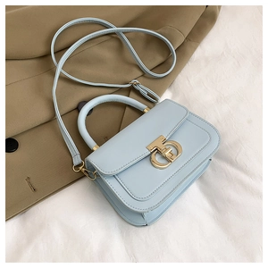 Détail d'un sac à bandoulière bleu clair avec boucle dorée sur un trench-coat