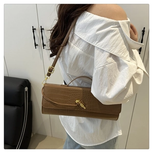 Detailed close-up of brown croc-effect baguette bag with golden knot buckle in use