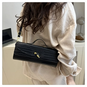 Detail of black crocodile texture baguette bag with golden metal twist lock and strap
