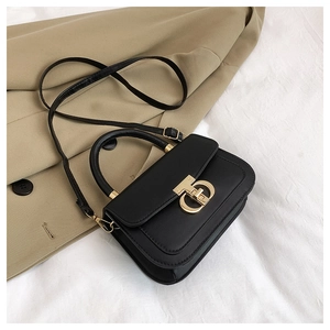 Détail d'un sac bandoulière noir avec fermoir doré géométrique sur tissu beige élégant