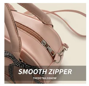 Close-up of smooth metal zipper and checkered bow ribbon on pink square handbag