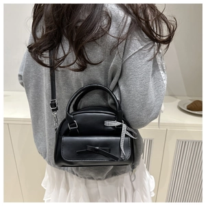 Detail of black semi-circular crossbody bag with leather bow and plaid ribbon on a model