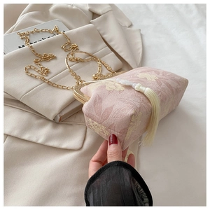 Gros plan sur un sac coquillage rose en tissu jacquard floral avec pompon blanc et chaîne