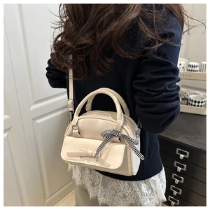 Detail of cream bow handbag with checkered ribbon on handle shown in a lifestyle setting