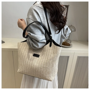 Detail of a large woven tote bag with black leather straps and a minimalist fashion tag