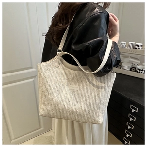 Detail of cream woven straw tote bag with FASHION patch and white leather strap
