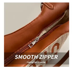 Detailed close-up of smooth silver metal zipper on a brown leather and woven shoulder bag