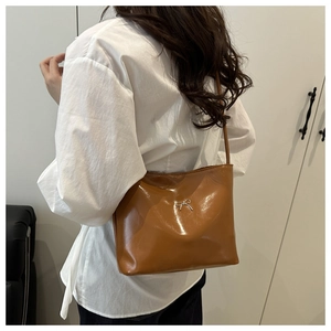 Detail view of brown glossy shoulder bag with a silver metal bow buckle on side