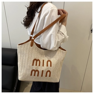 Detail of a large woven tote bag with brown straps and logo on a chic shoulder model
