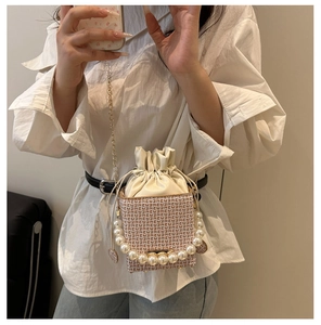 Detail of woven crossbody bag with pearl handle and golden chain strap on white outfit