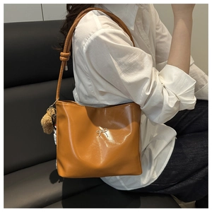 Close-up of caramel PU leather tote bag with silver bow buckle and pompom charm detail