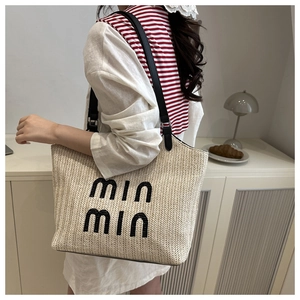 Detail of beige woven straw tote bag with black letter embroidery and leather shoulder strap