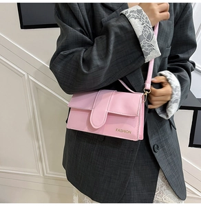 Pink leather crossbody bag detail with golden fashion lettering shown on a model