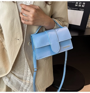 Detail of light blue patent leather handbag featuring gold fashion lettering and handle