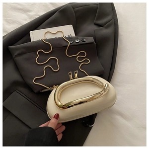 Détail d'une pochette demi-lune blanc crème avec anse anneau doré sur un blazer noir