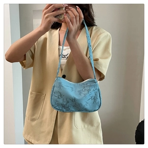 Close-up of light blue floral underarm bag with blue leaf print on satin fabric