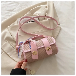 Detail of cylindrical woven crossbody bag featuring pink leather trim and dual gold clasps