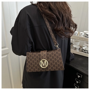 Bolso bandolera clásico marrón con monograma y hebilla dorada en M usado por modelo